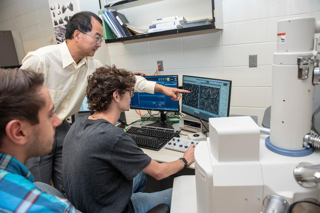 Professor and students working on a computer in an engineering lab.