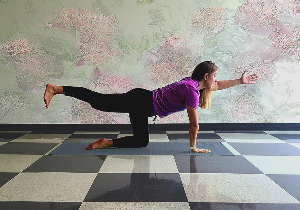 Health coach demonstating the bird dog yoga pose on a gray mat with pastel muted wall in the background and a white and black checkered floor