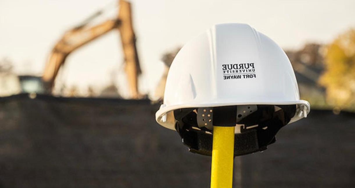 Construction helmet on a shovel with a backhoe in the background